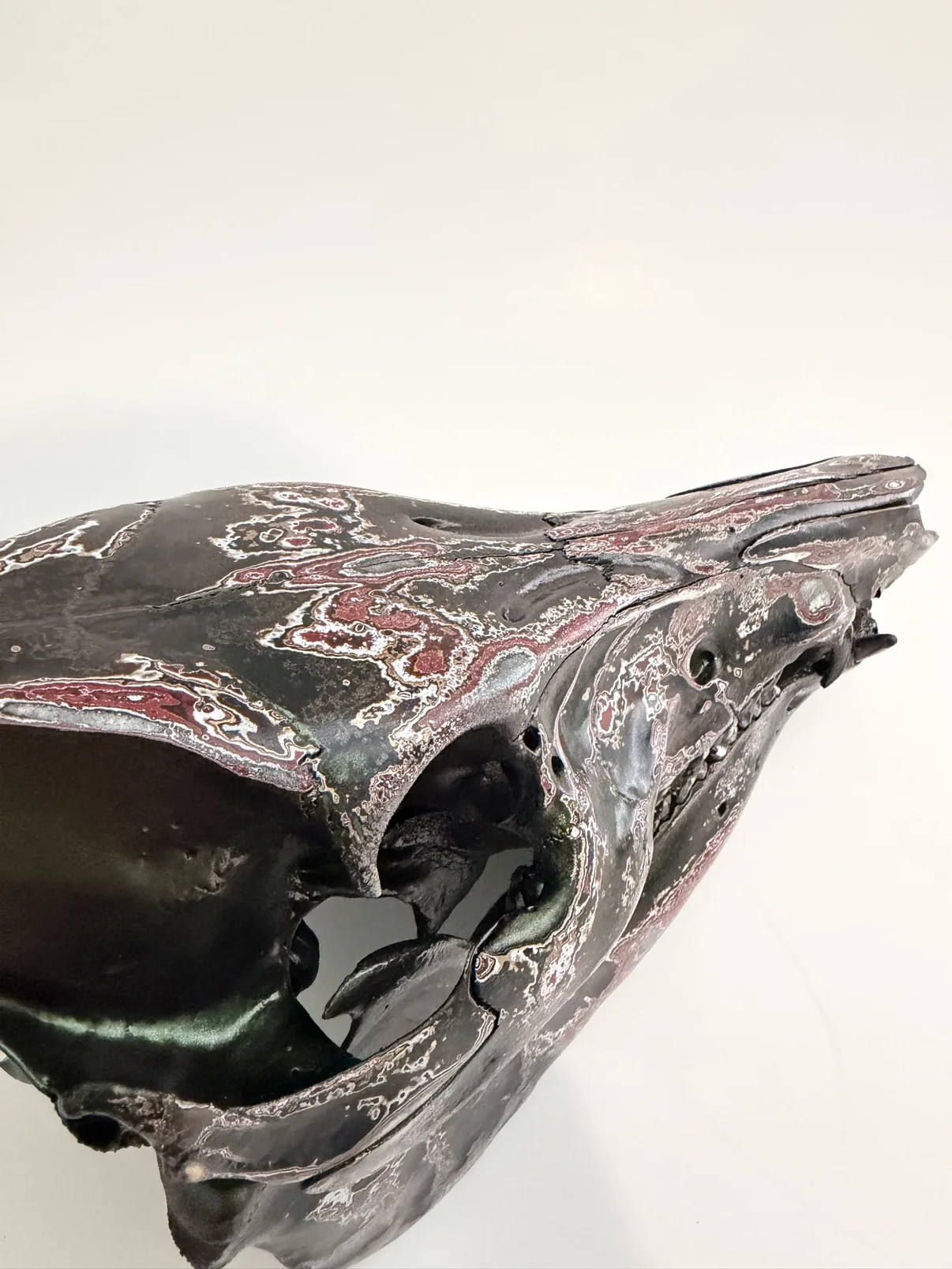 Close-up photograph of the side of my hand-painted feral hog skull, showing the layered burgundy, silver and black fordite finish around the eye socket