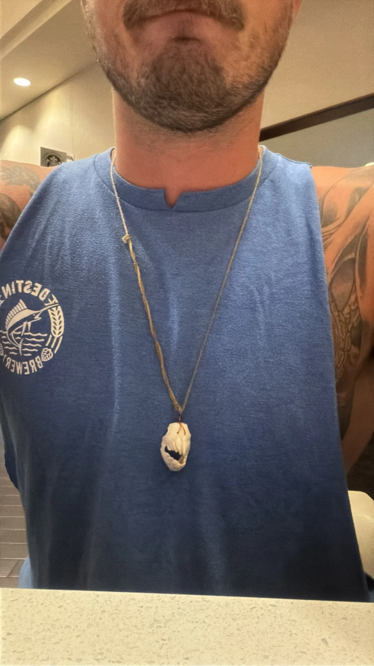 Photograph of a man wearing one of my triggerfish jaw necklaces on a long light cord over a blue tank top, the white bone jaw pendant at his chest