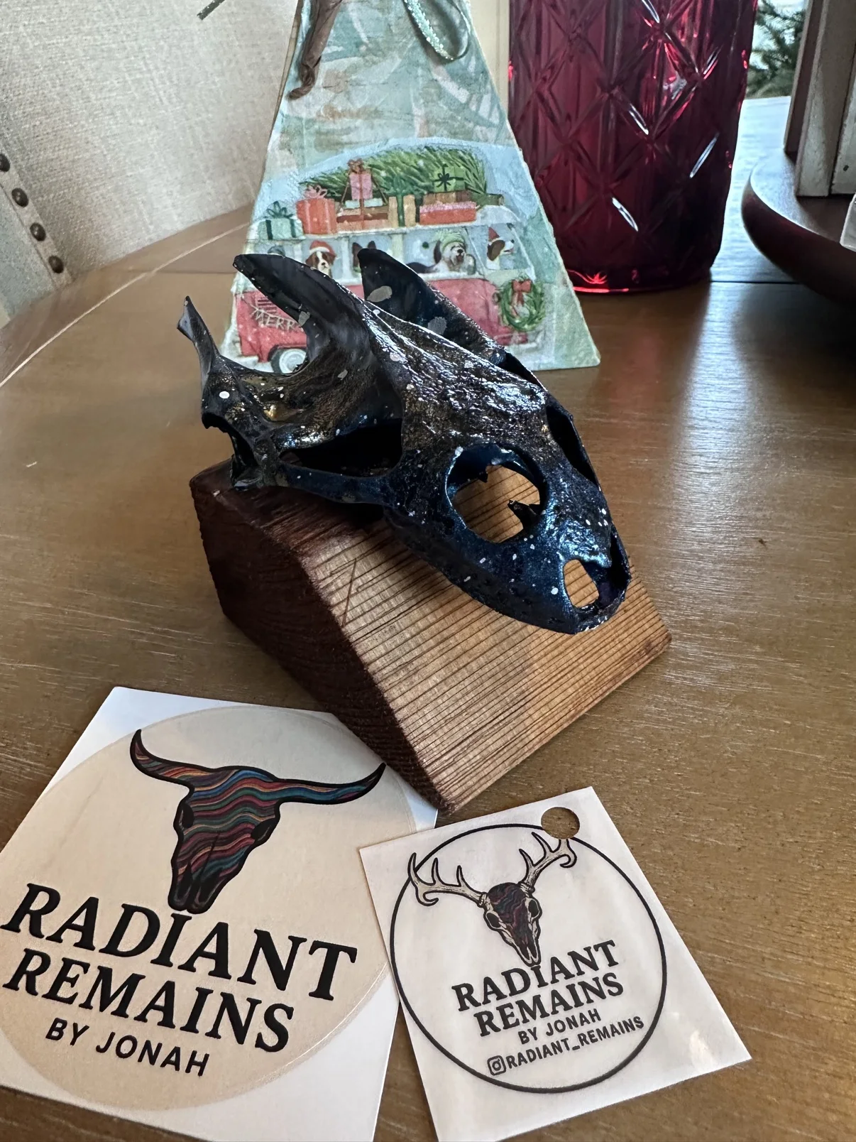 Photograph of my small hand-painted skull in dark iridescent blue and green on its wooden stand, sitting on a table