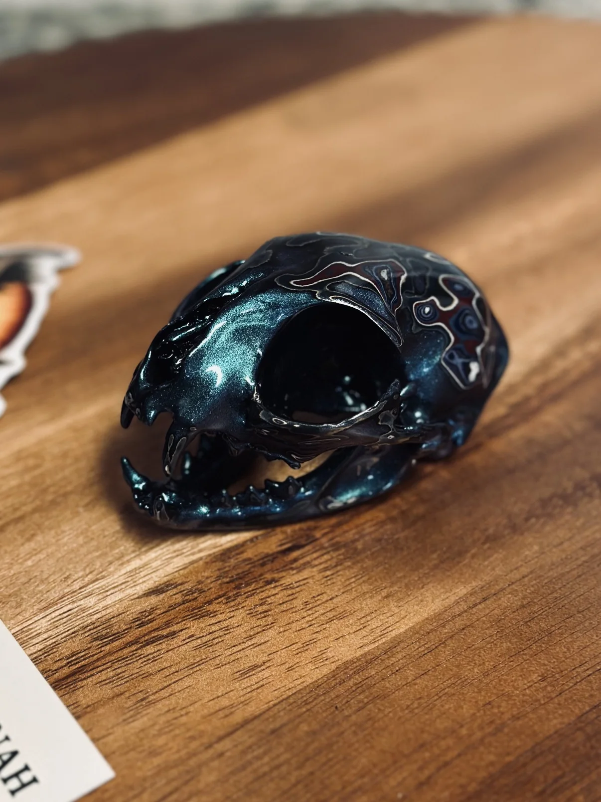 Photograph of my small hand-painted animal skull from the side on a wooden board, showing the jaw and the dark teal metallic finish